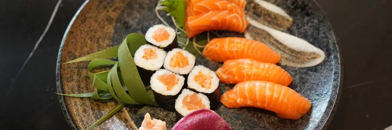 Salmon nigiri, maki and sashimi on a dark plate