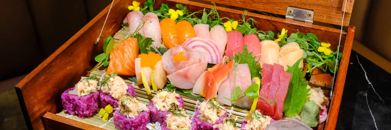 A wooden box of sashimi and sushi with edible flowers