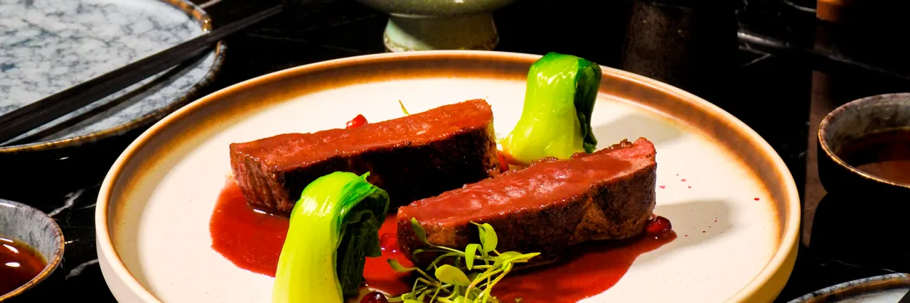 Sliced beef with pak choi and a red sauce on a white plate