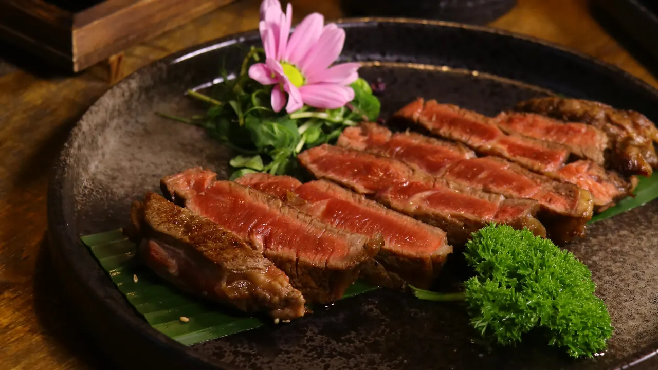 Sliced seared beef on a stone plate with a flower and parsley