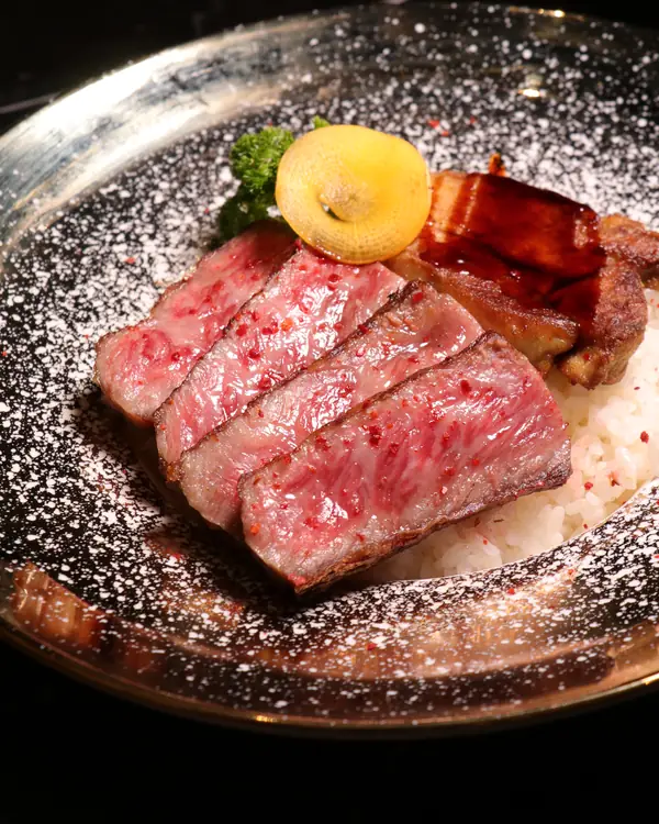 Slices of marbled Wagyu ribeye with seared foie gras over rice, on a plate dusted white