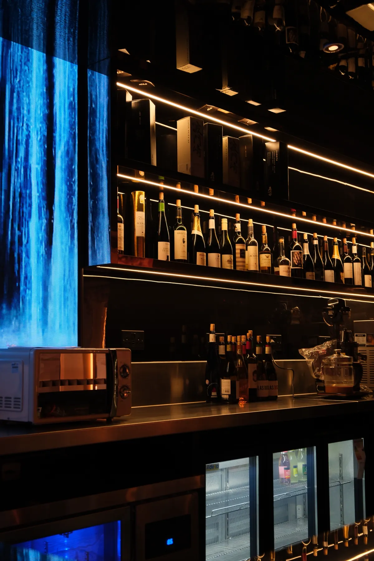The bar lit in gold, shelves of sake and whisky beside a wall of falling water