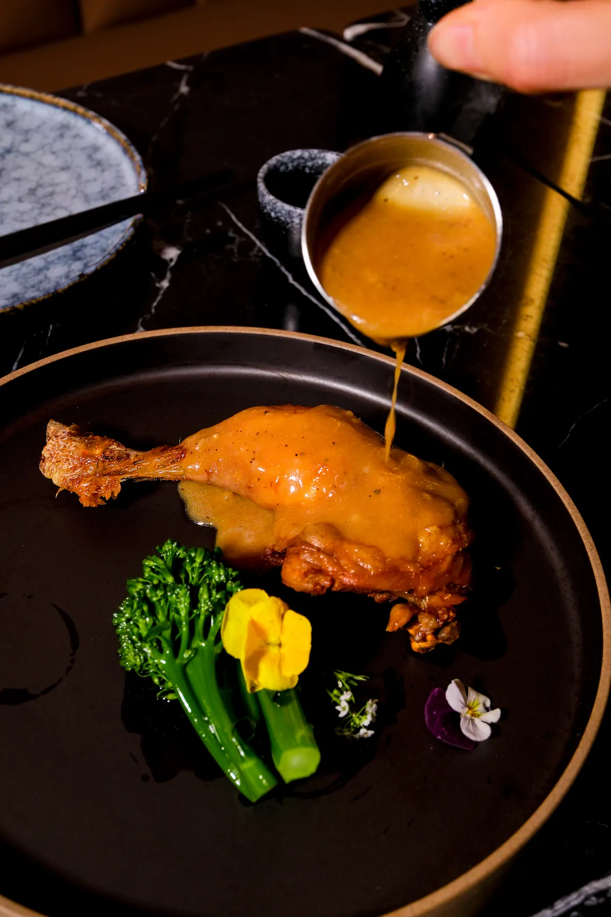 Sauce poured over a roast duck leg with tenderstem broccoli