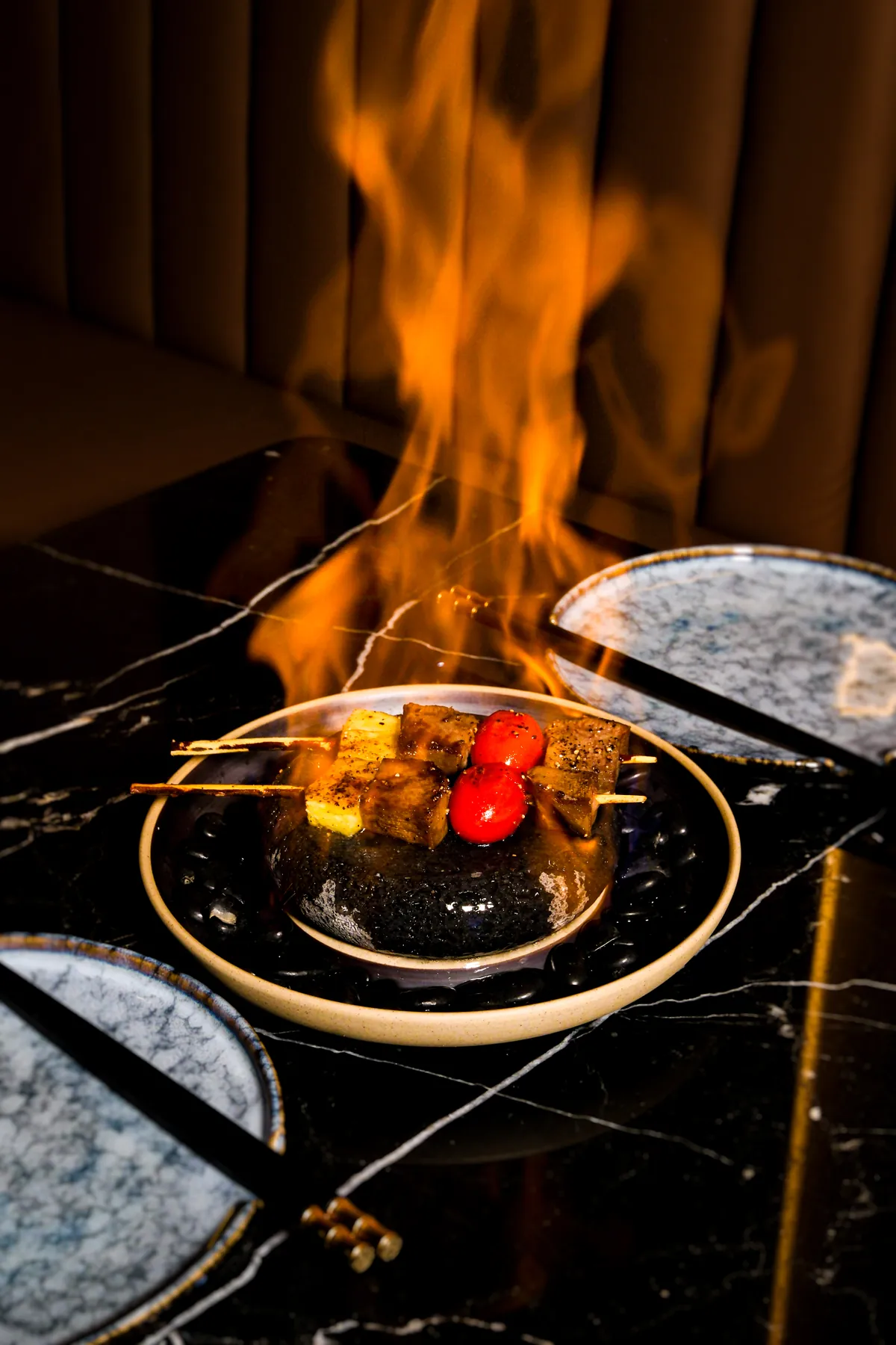 Skewers of beef and tomato under a tall flame at the table