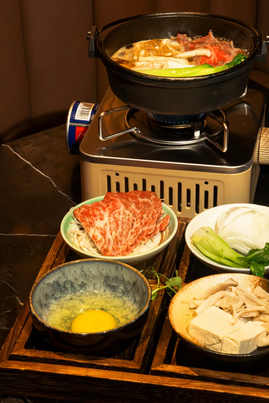 A Wagyu hot pot on its burner, with marbled beef, a raw egg, tofu and mushrooms laid out beside it