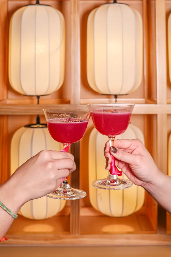 Two guests raising pink cocktails under the paper lantern wall