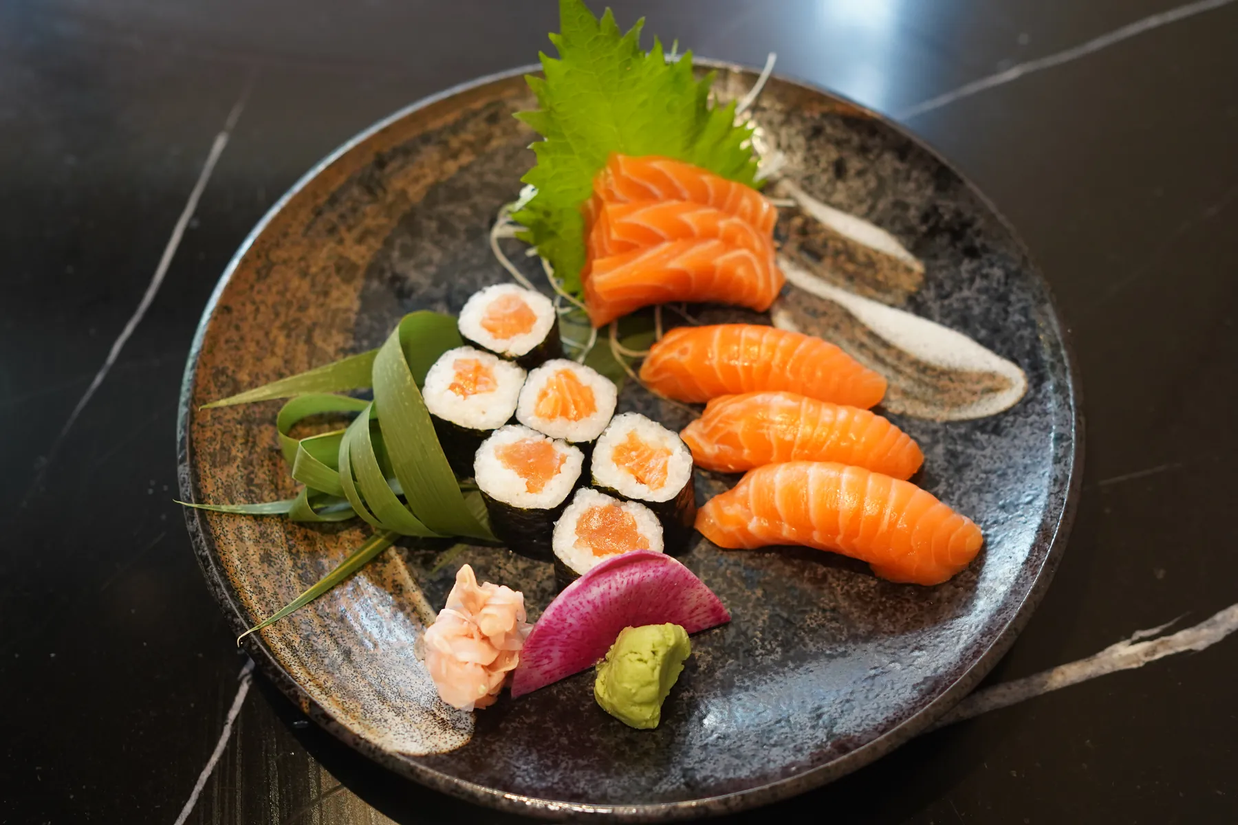 Salmon sashimi, nigiri and maki on a dark plate, with pickled ginger and wasabi